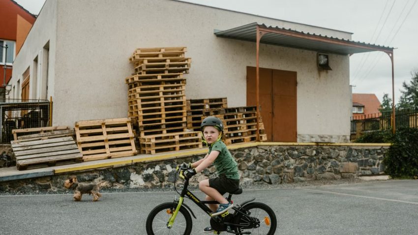 Young boy with helmet riding a bicycle outside an industrial building.